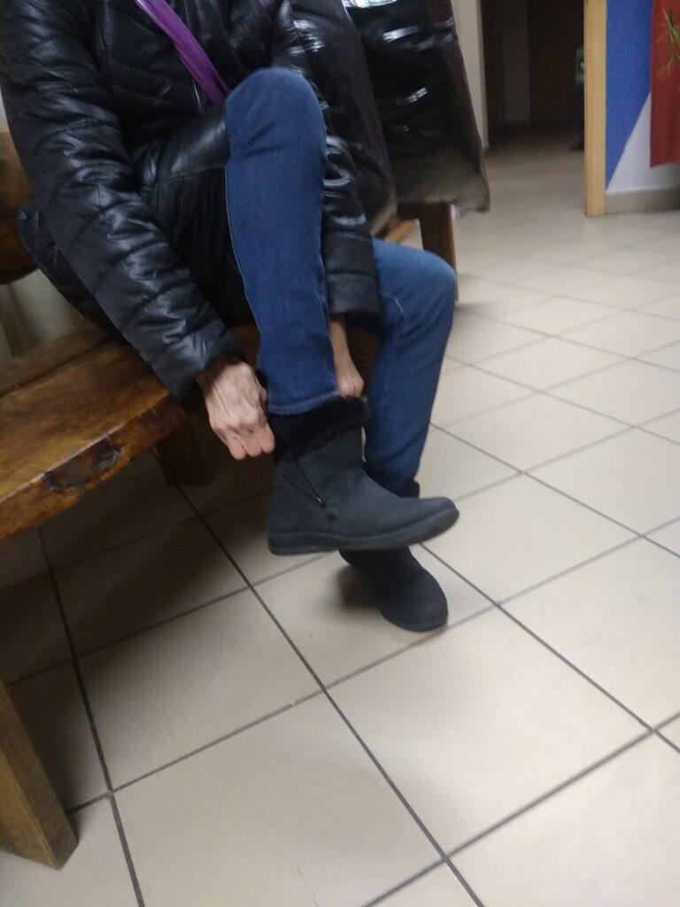 Kobieta siedząca na ławce i zakładająca zimowego buta.