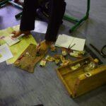 Osoba malująca obraz stopami, trzymająca pędzel w jednej stopie i przytrzymująca kartę drugą stopą.