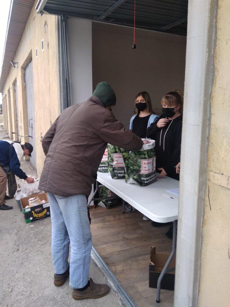 Mężczyzna odbierający reklamówki z produktami spożywczymi przekazane w ramach pomocy.