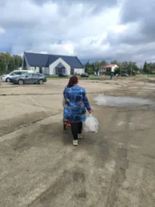 Kobieta z wózkiem i reklamówkami z pomocą żywnościową na tle kościoła.