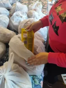 Kobieta przy stole pakuje artykuły spożywcze do torby dla osób potrzebujących.
