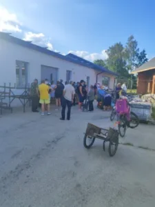 Osoby stoją przed budynkiem, rozmawiają i czekają na wydanie darów.
