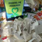 Przezroczyste pudełko z paragonami z akcji „Podziel się posiłkiem” wyłożonymi na stole.
