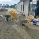 Betoniarka i taczka z piaskiem wykorzystywane podczas dobudowy pomieszczenia.