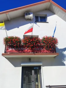Balkon domu ozdobiony transparentem Błogosławiona Krew Jezusowa.