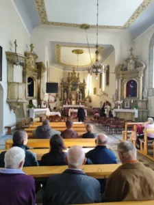 Pielgrzymi siedzący w ławkach we wnętrzu kościoła św. Michała.